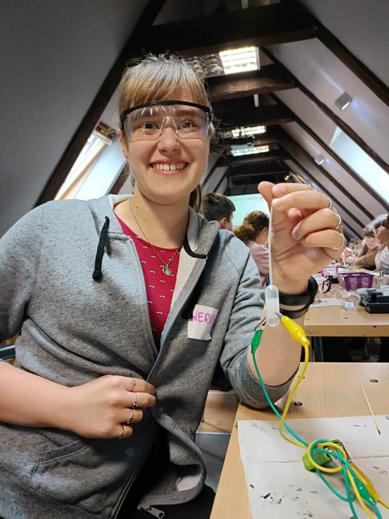 Trzymam w dłoni obwód elektryczny podłączony do baterii 9 woltowej, połączony z probówka, w której znajduje się roztwór wodny NaCl