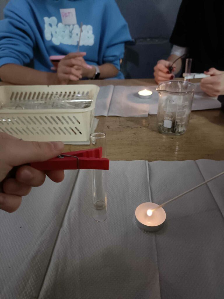 Perhydrol w stężeniu 15% wraz z kilkoma kroplami nadmanganianu potasu KMnO4, obok tealight z podpalonym łuczywem